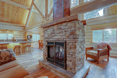 Example of a huge mountain style open concept laminate floor and brown floor living room design in Other with brown walls, a two-sided fireplace and a stone fireplace