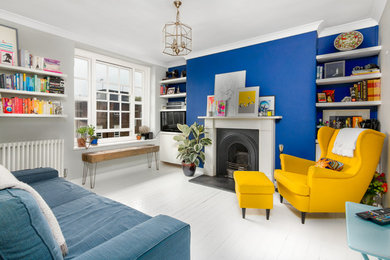 Abgetrenntes Modernes Wohnzimmer mit blauer Wandfarbe, gebeiztem Holzboden, Kamin, Kaminumrandung aus Holz und weißem Boden in Surrey