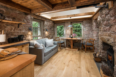 Cette photo montre un petit salon nature fermé avec un poêle à bois, un manteau de cheminée en pierre, un téléviseur fixé au mur, un mur marron et parquet clair.