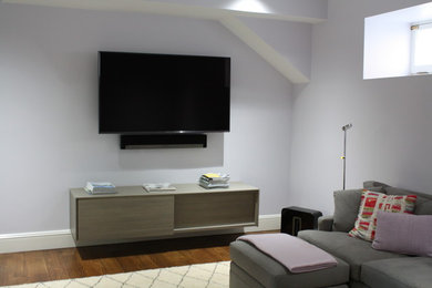 Immagine di un soggiorno contemporaneo di medie dimensioni con sala formale, pareti grigie, pavimento in legno massello medio, TV a parete e pavimento marrone