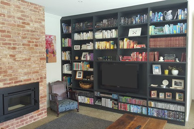 Ejemplo de biblioteca en casa abierta minimalista grande con paredes negras, suelo de cemento, todas las chimeneas, marco de chimenea de ladrillo y pared multimedia
