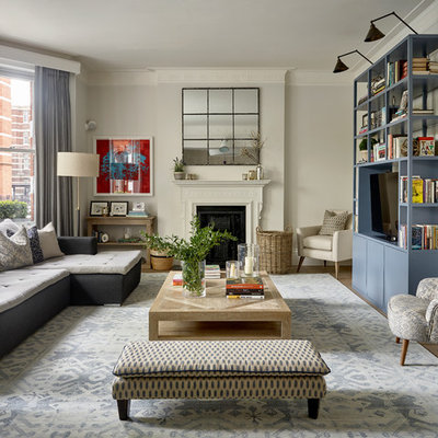 Example of a mid-sized transitional enclosed medium tone wood floor and brown floor living room design in London with gray walls, a standard fireplace, a plaster fireplace and a media wall