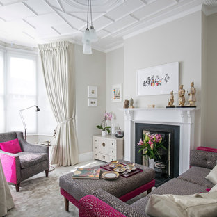 Traditional enclosed living room in London with a reading nook, beige walls, carpet, a standard fireplace, a wooden fireplace surround, a concealed tv and beige floors.