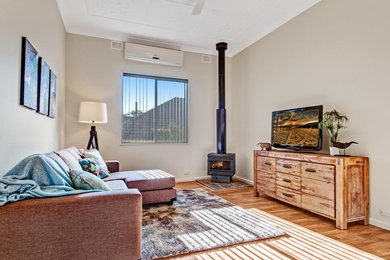 Ejemplo de salón abierto actual de tamaño medio con paredes beige, suelo de madera en tonos medios, estufa de leña, marco de chimenea de metal y televisor independiente