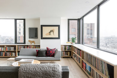 Diseño de biblioteca en casa abierta contemporánea de tamaño medio sin televisor con paredes blancas, suelo de madera clara y suelo beige
