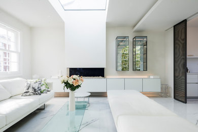 Photo of a contemporary living room in London with white walls, ceramic flooring, a hanging fireplace, a tiled fireplace surround and white floors.