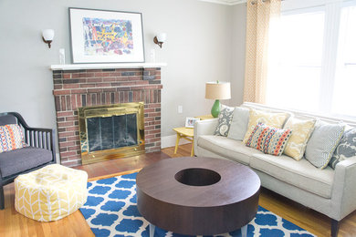 Mid-sized eclectic formal and open concept medium tone wood floor living room photo in Boston with gray walls, a standard fireplace, a brick fireplace and a tv stand