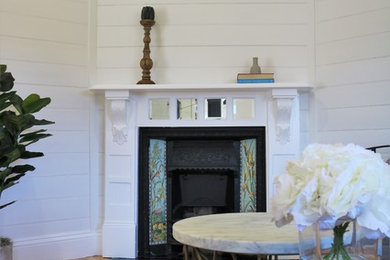 Modelo de salón cerrado tradicional renovado de tamaño medio con paredes blancas, suelo de madera clara, chimenea de esquina, marco de chimenea de madera y suelo beige