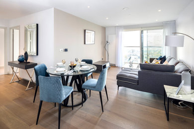 This is an example of a large contemporary formal open plan living room in London with white walls, medium hardwood flooring, no fireplace, no tv and brown floors.