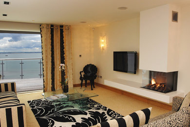 This is an example of a large contemporary enclosed living room in Essex with beige walls, light hardwood flooring, a two-sided fireplace, a plastered fireplace surround and a wall mounted tv.