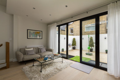 This is an example of a contemporary open plan living room in London with beige walls and medium hardwood flooring.