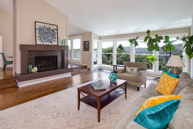 Photo of a large classic living room in Santa Barbara with beige walls, medium hardwood flooring, a two-sided fireplace, a tiled fireplace surround and brown floors.