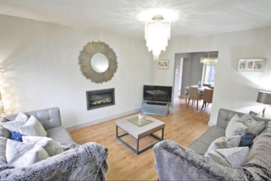 Medium sized contemporary formal enclosed living room in Essex with grey walls, laminate floors, a ribbon fireplace, a metal fireplace surround, a freestanding tv and brown floors.