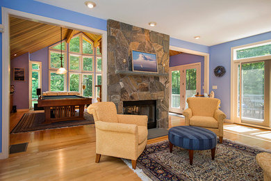 Diseño de biblioteca en casa abierta clásica de tamaño medio sin televisor con paredes azules, suelo de madera en tonos medios, chimenea de doble cara y marco de chimenea de piedra