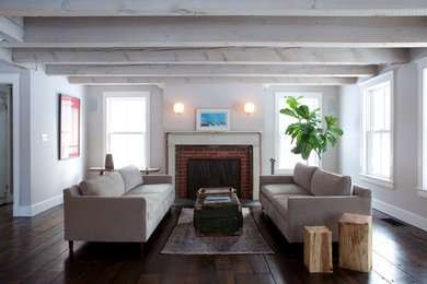 Abgetrenntes Country Wohnzimmer mit weißer Wandfarbe, dunklem Holzboden, Kamin und Kaminumrandung aus Backstein in New York