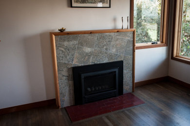 Bild på ett mellanstort funkis allrum med öppen planlösning, med vita väggar, mellanmörkt trägolv, en standard öppen spis, en spiselkrans i trä och grått golv