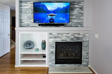 デンバーにある低価格の中くらいなおしゃれなLDK (無垢フローリング、標準型暖炉、石材の暖炉まわり、壁掛け型テレビ、茶色い床) の写真