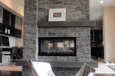 エドモントンにある中くらいなトランジショナルスタイルのおしゃれなLDK (ベージュの壁、無垢フローリング、両方向型暖炉、石材の暖炉まわり、茶色い床、テレビなし) の写真