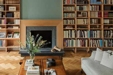 Foto de biblioteca en casa abierta pequeña con paredes verdes, suelo de madera clara, todas las chimeneas y marco de chimenea de piedra