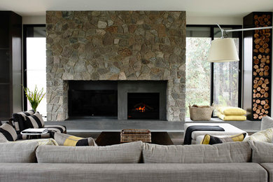 Foto de salón abierto contemporáneo de tamaño medio con paredes grises, suelo de madera en tonos medios, marco de chimenea de piedra y televisor colgado en la pared