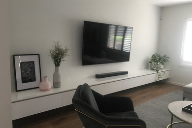 Imagen de salón moderno grande con paredes blancas, suelo de madera pintada y televisor colgado en la pared