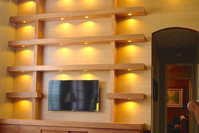 Diseño de biblioteca en casa abierta actual de tamaño medio con paredes beige, suelo de madera en tonos medios y televisor colgado en la pared