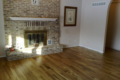 Inspiration for a large timeless medium tone wood floor living room remodel in Other with white walls, a standard fireplace and a brick fireplace