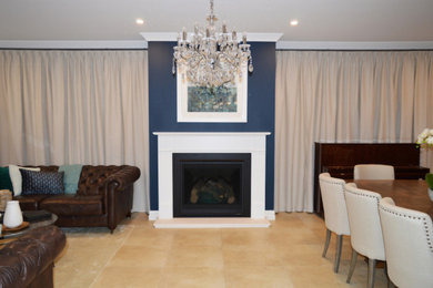 На фото: большая парадная, открытая гостиная комната в стиле неоклассика (современная классика) с синими стенами, полом из травертина, стандартным камином, фасадом камина из дерева и бежевым полом с