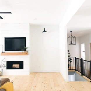 Großes Country Wohnzimmer mit weißer Wandfarbe, hellem Holzboden, Kamin, Kaminumrandung aus Holzdielen und Multimediawand in Tampa