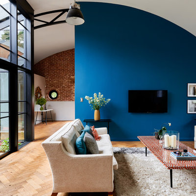 Example of a huge trendy open concept brown floor and medium tone wood floor living room design in Hampshire with blue walls, no fireplace and a wall-mounted tv