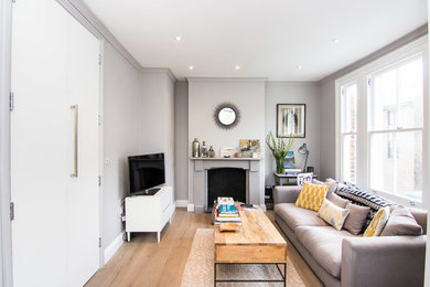 Idées déco pour un salon moderne de taille moyenne et ouvert avec un mur gris, parquet clair, une cheminée standard, un manteau de cheminée en bois et un téléviseur indépendant.