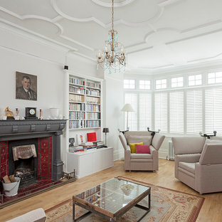 This is an example of a medium sized classic living room in London with a reading nook, white walls, a metal fireplace surround, beige floors, light hardwood flooring and a standard fireplace.