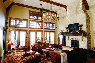 Cette photo montre un grand salon montagne ouvert avec un mur beige, parquet foncé, une cheminée standard, un manteau de cheminée en pierre, un téléviseur fixé au mur et un sol marron.