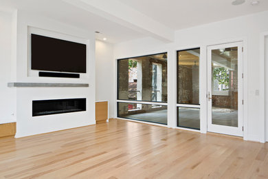 Diseño de salón contemporáneo con paredes blancas, suelo de madera clara, chimenea lineal y televisor colgado en la pared