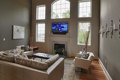 Foto de salón cerrado tradicional grande con paredes grises, suelo de madera clara, todas las chimeneas, marco de chimenea de piedra y televisor colgado en la pared