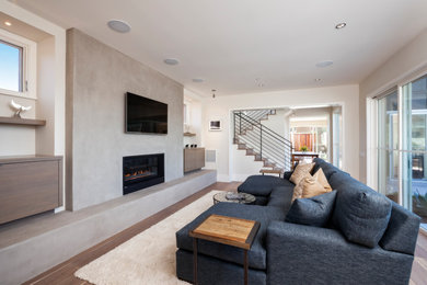 Mid-sized trendy open concept medium tone wood floor and brown floor living room photo in San Francisco with white walls, a standard fireplace, a concrete fireplace and a wall-mounted tv