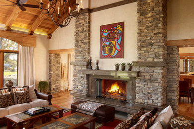 Modelo de salón para visitas abierto rural sin televisor con paredes beige, suelo de madera en tonos medios, todas las chimeneas y marco de chimenea de piedra