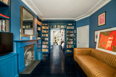 Photo of a traditional living room in London with blue walls, painted wood flooring, a standard fireplace, a wooden fireplace surround and black floors.