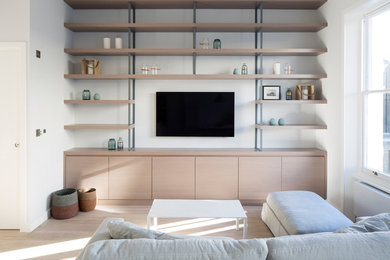 Modelo de salón para visitas abierto moderno grande con paredes grises, suelo de madera clara y televisor colgado en la pared