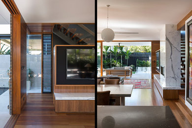 Diseño de salón abierto actual con paredes blancas, suelo de madera en tonos medios, marco de chimenea de piedra y pared multimedia