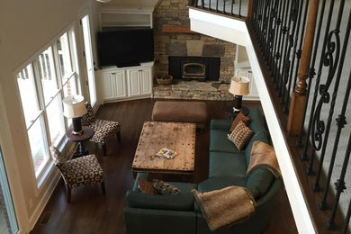 Cette image montre un grand salon ouvert avec un mur beige, un sol en bois brun, une cheminée standard, un manteau de cheminée en pierre, un téléviseur encastré et un sol marron.