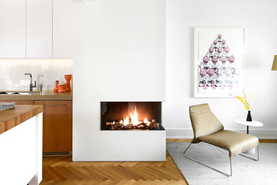 バンクーバーにある高級な中くらいなトランジショナルスタイルのおしゃれなリビング (白い壁、淡色無垢フローリング、コーナー設置型暖炉、漆喰の暖炉まわり、テレビなし) の写真
