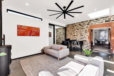 Diseño de salón abierto contemporáneo grande con paredes blancas, suelo de cemento, estufa de leña, marco de chimenea de ladrillo y suelo gris