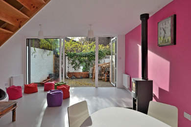 Contemporary open plan living room in London with pink walls and a wood burning stove.