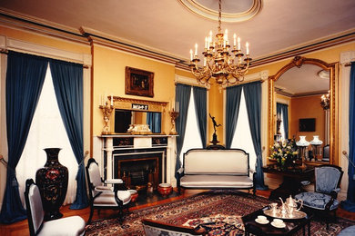 Immagine di un soggiorno vittoriano chiuso con pareti gialle, parquet scuro, camino classico e cornice del camino in intonaco