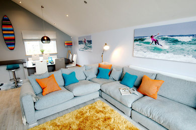 Large beach style open plan living room in Cornwall with blue walls, light hardwood flooring and grey floors.