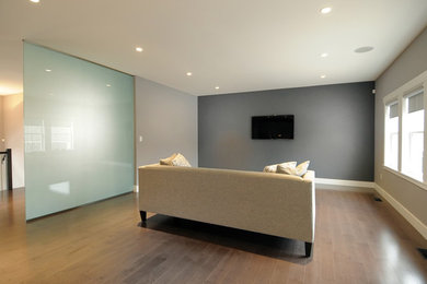 Diseño de salón cerrado moderno con paredes grises, suelo de madera en tonos medios y televisor colgado en la pared