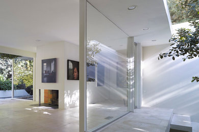Example of a trendy loft-style travertine floor and white floor living room design in Los Angeles with white walls, a standard fireplace and a plaster fireplace
