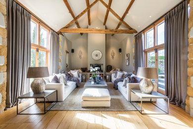 Foto de salón para visitas abierto campestre de tamaño medio con paredes grises, suelo de madera clara, estufa de leña, suelo beige y cortinas