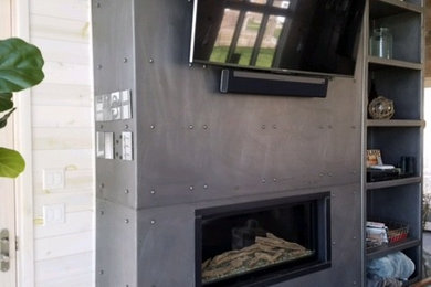 Modelo de salón abierto industrial de tamaño medio con paredes blancas, suelo de cemento, chimenea lineal, marco de chimenea de metal, televisor colgado en la pared y suelo gris